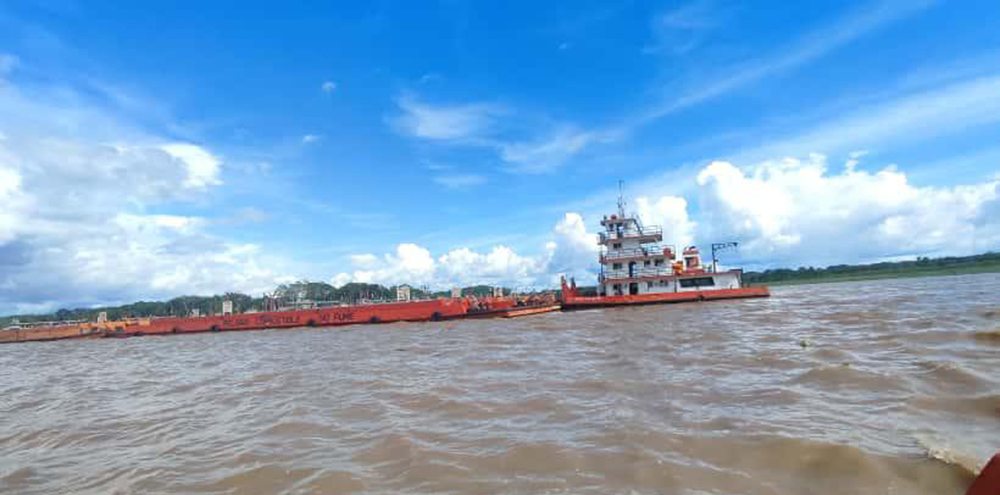 Convoy de barcazas y empujador navegando el río bajo cielo azul